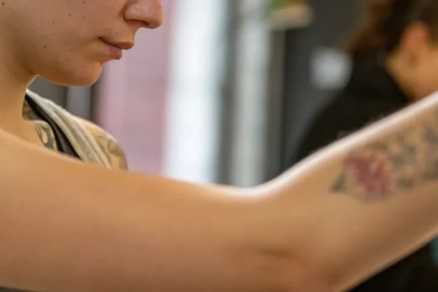 Young woman looking at her arm post-tattoo removal, ready for a new tattoo, in a tattoo studio setting.